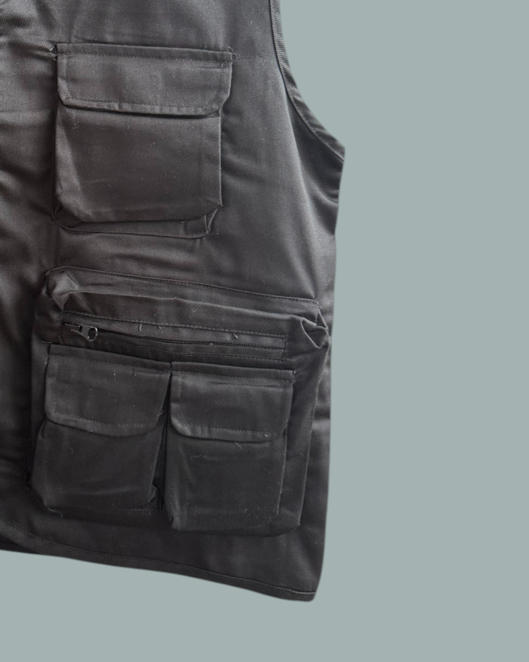 En Lucky Bait Fiskeväst med flera framfickor och dragkedjor, där endast den vänstra sidan syns. Visas mot en stålblå bakgrund.