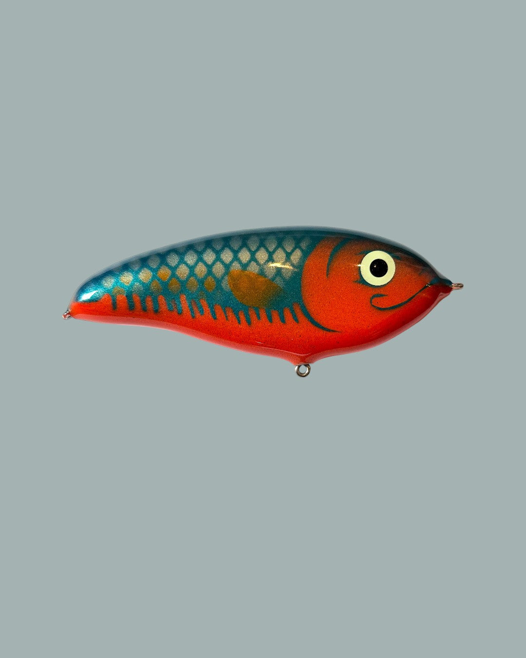 Ett färgstarkt Lucky Bait Limited Edition bete-fiskedrag, format som en fisk med röd undersida, blå topp, fjälsmönster och serietidningsliknande öga. Visas mot en stålblå bakgrund.