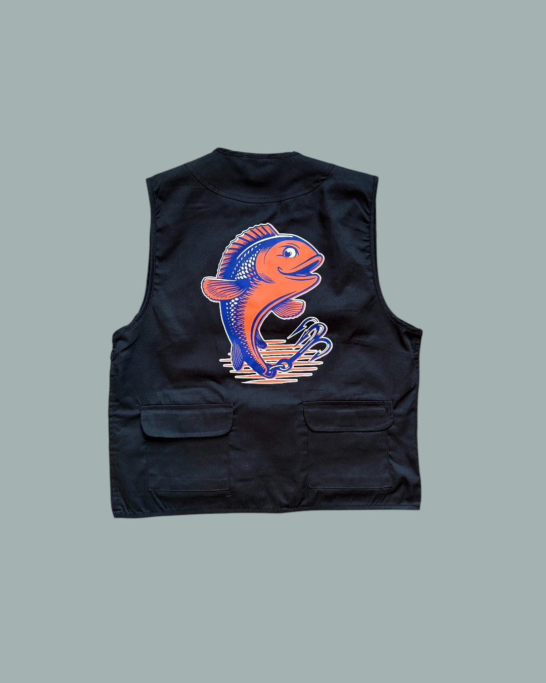 Fiskevästen är en svart fiskeväst med två framfickor och en färgglad orange och blå fiskillustration  på baksidan. Visas mot en stålblå bakgrund.