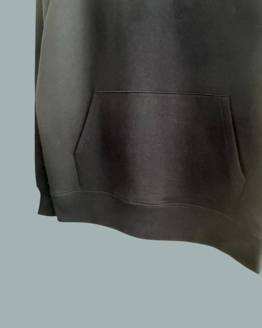 En närbild av Lucky Bait Hoodie Svart med känguruficka fram. Visas mot en stålblå bakgrund.