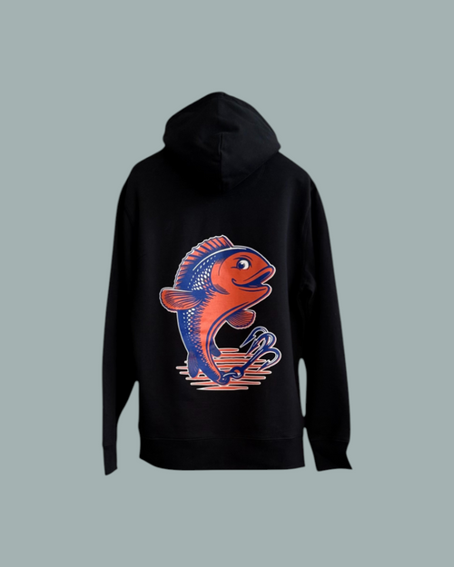 Hoodie Svart: svart hoodie med stor, färgstark logo av en rödblå fisk som hoppar ovanför stiliserade våglinjer på ryggen. Visas mot en stålblå bakgrund.