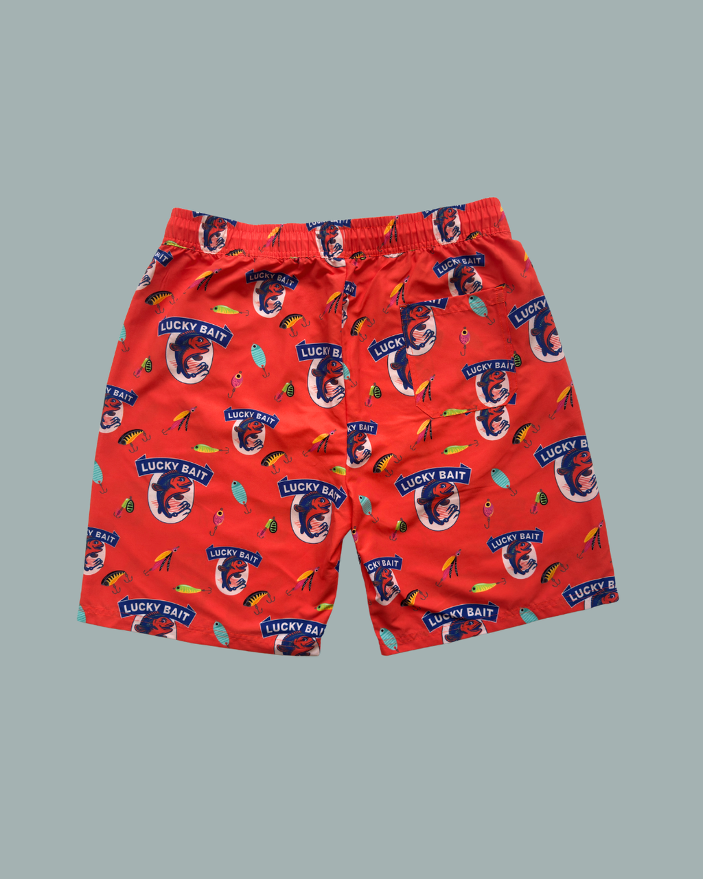 Lucky Bait Shops ”Lucky bait Badbrallor” är röda, färgglada badshorts för män med lekfulla fiskar, fiskebeten och texten ”LUCKY BAIT” tryckt över hela plagget på en ljusgrå bakgrund.